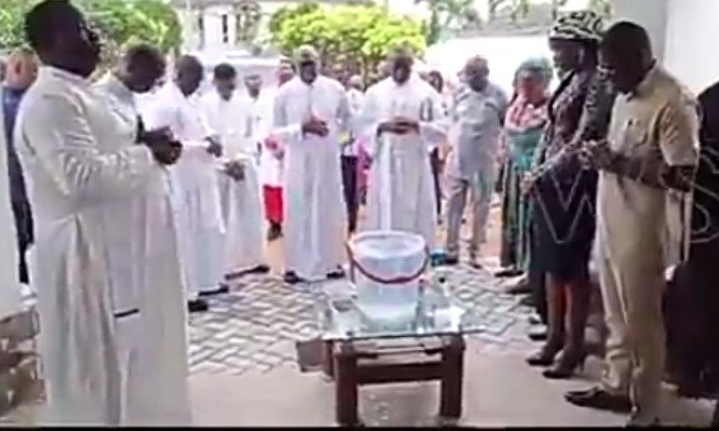 Moment Priest Sprinkles ‘Holy Water’ On Shaibu At Office Dedication